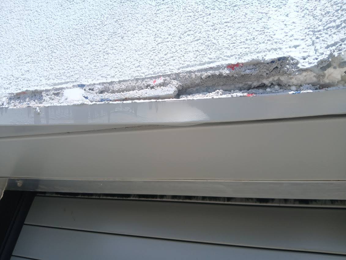 Close view of failed exterior finish above a roll-up door