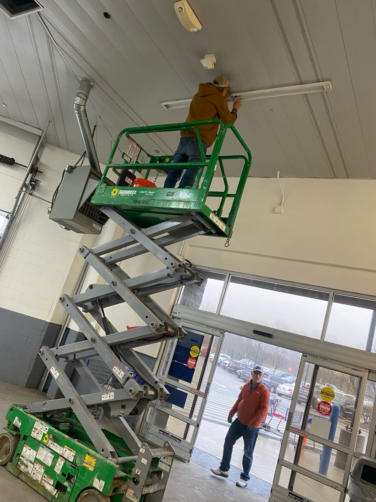 Technician servicing a commercial light fixture from a lift