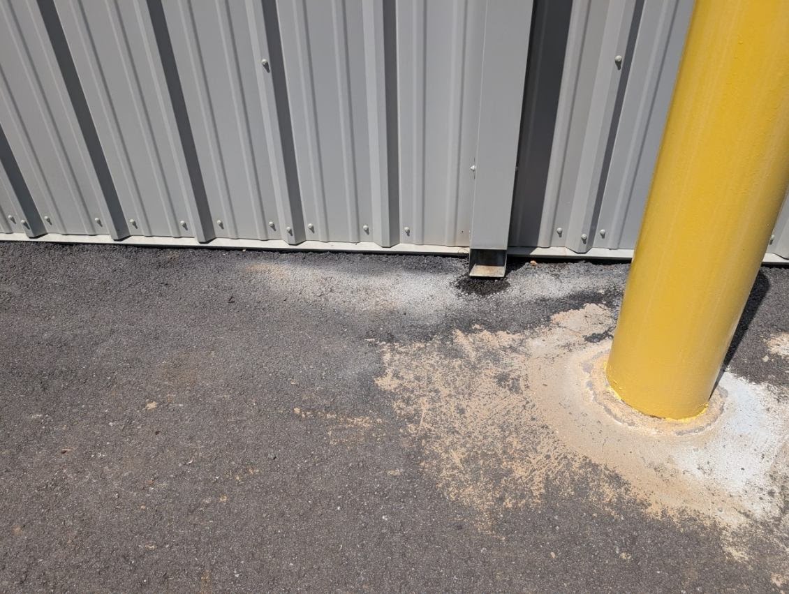 Exterior downspout terminating beside an asphalt surface